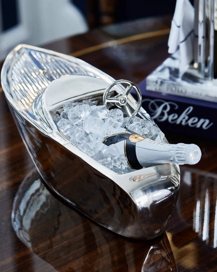 Champagne bottle in a decorative boat-shaped ice bucket on a table.