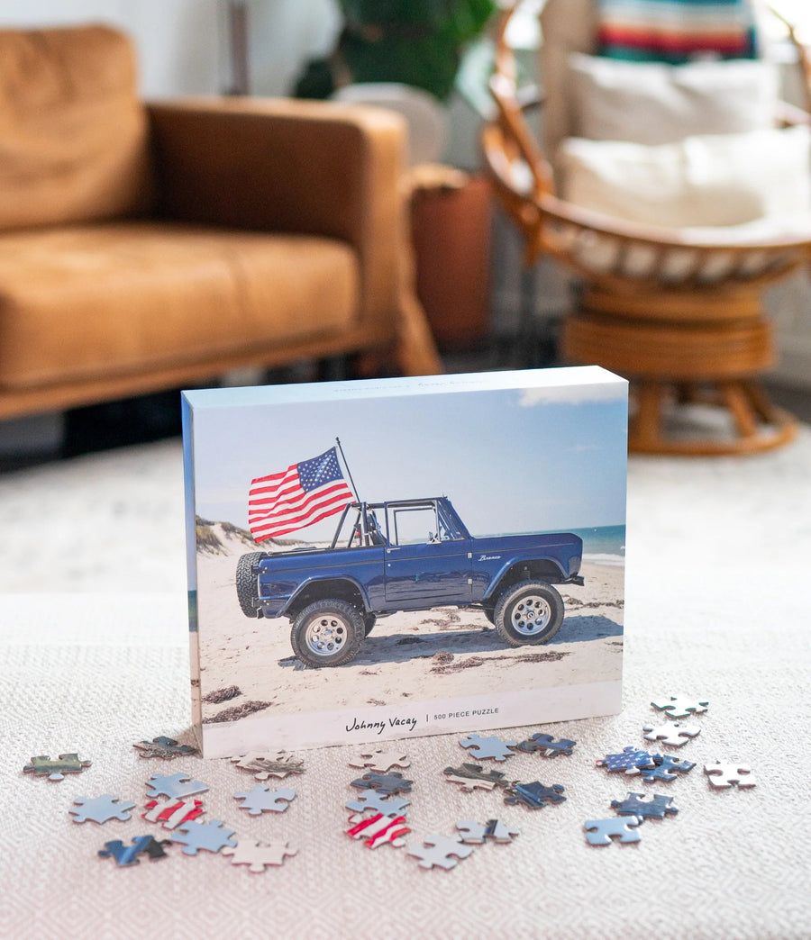 Puzzle box with a blue truck and American flag design, surrounded by scattered puzzle pieces on a light-colored surface.