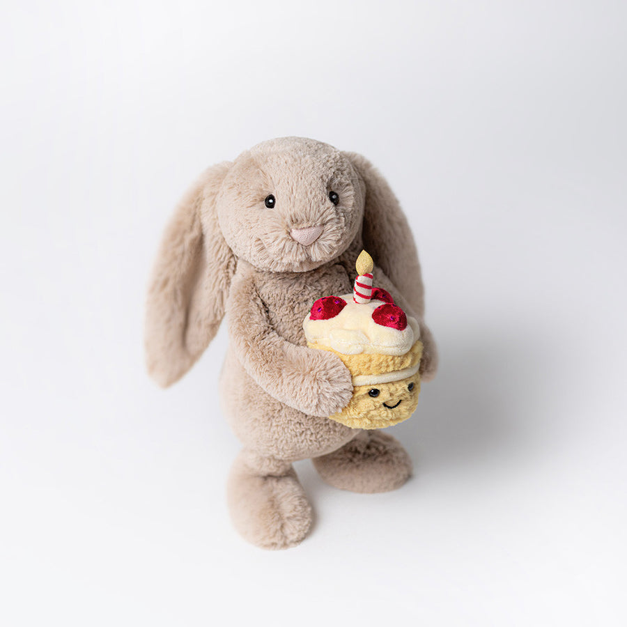 Plush toy rabbit holding a cupcake with a candle on a white background