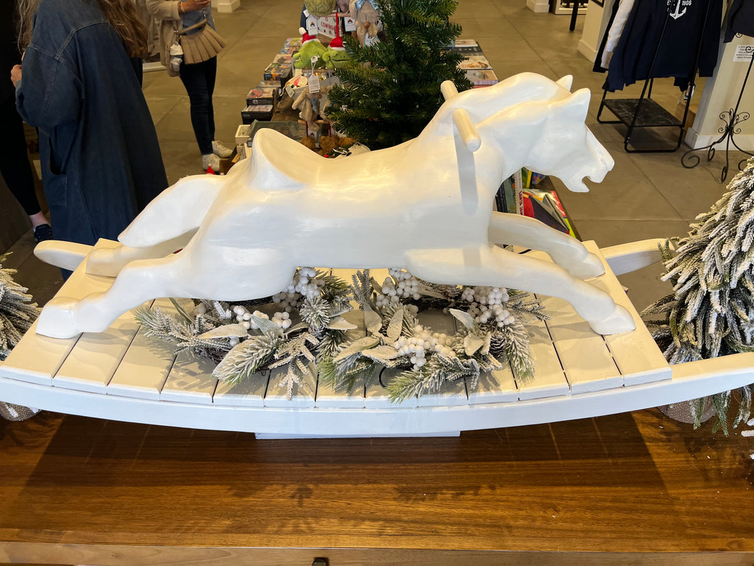 Decorative display with white horse sculptures on a wooden base in a store setting.