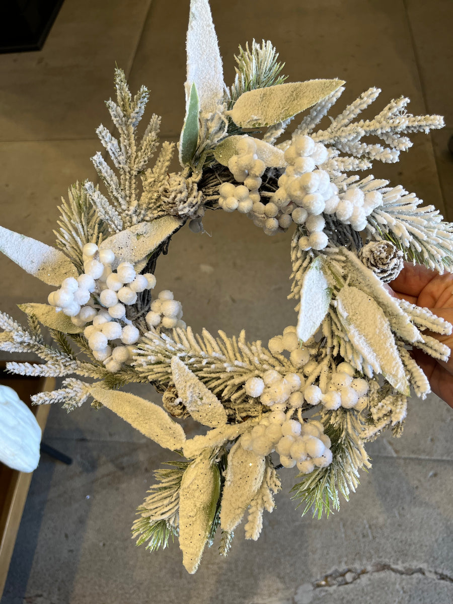 Decorative wreath with artificial greenery and white berries on a neutral background
