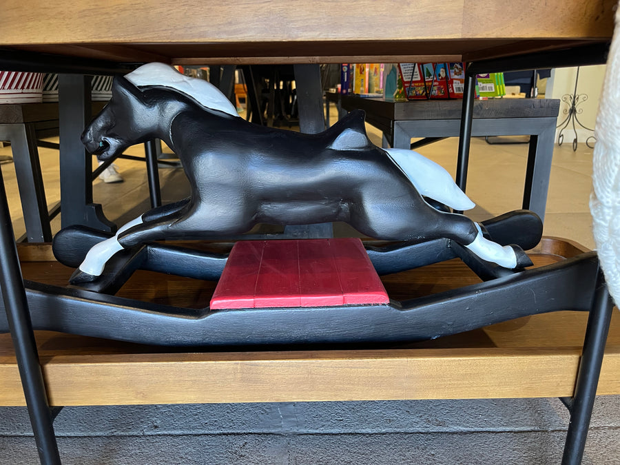 Black dog figurine under a wooden table with a blurred indoor background