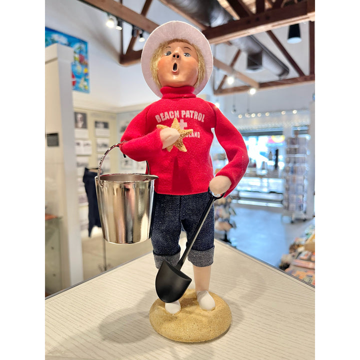 Figurine of a child in a red 'Beach Patrol' shirt holding a shovel and bucket in a store setting.